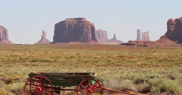 Old wooden wagon in a desert landscape with Monument Valley rock formations in Utah, ideal for outdoor adventure enthusiasts and nature lovers.