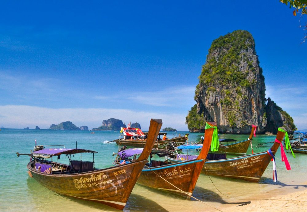 Longtail boats on Railay Beach framed by tall limestone cliffs in Krabi, Thailand